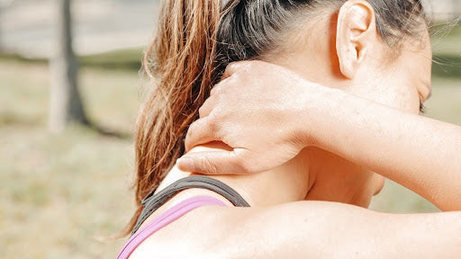 Woman outdoors reaching behind her neck to scratch an insect bite on her upper back.